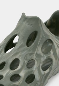 Zapato slip-on ligero de color verde oliva con un diseño texturizado y perforado que presenta grandes cortes ovalados y un logo grabado en el lateral.