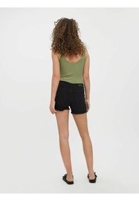 Grön tanktop och svarta denimshorts med fransad fåll, slim fit, svarta sandaler. Modell vänd bort, visar bakifrån och frisyr.