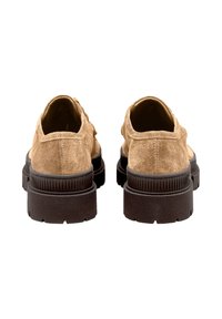 Une paire de chaussures à plateforme en suede beige vues de l'arrière, avec des semelles épaisses noires texturées sur un fond blanc.