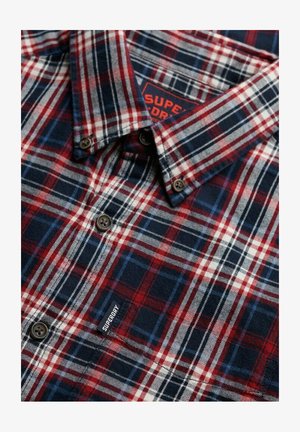 Camisa de cuadros rústica hecha de franela, con colores rojo, marino y blanco. Incluye cierres de botones y una pequeña etiqueta de marca en la parte delantera.