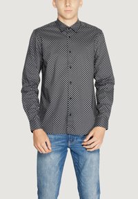 Camicia a maniche lunghe a motivi bianco e nero con colletto a bottoni, caratterizzata da un design geometrico e una texture liscia, abbinata a jeans blu.