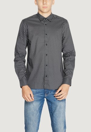 Camicia a maniche lunghe a motivi bianco e nero con colletto a bottoni, caratterizzata da un design geometrico e una texture liscia, abbinata a jeans blu.