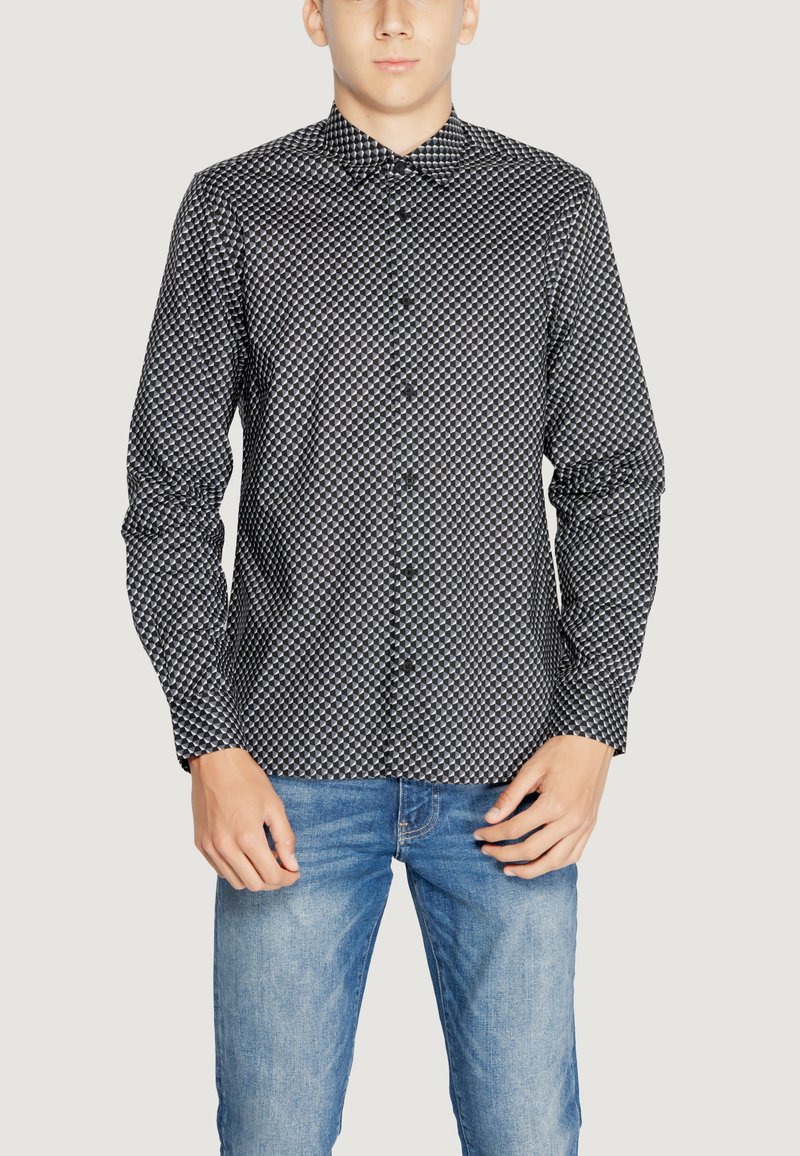 Camicia a maniche lunghe a motivi bianco e nero con colletto a bottoni, caratterizzata da un design geometrico e una texture liscia, abbinata a jeans blu.