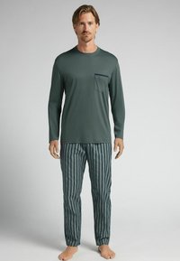 Dlouhý rukáv zeleného trika s kapsou na prsou v kombinaci s modrými a světle zelenými pruhovanými kalhotami. Měkká tkanina, uvolněný střih, jednoduchý design.