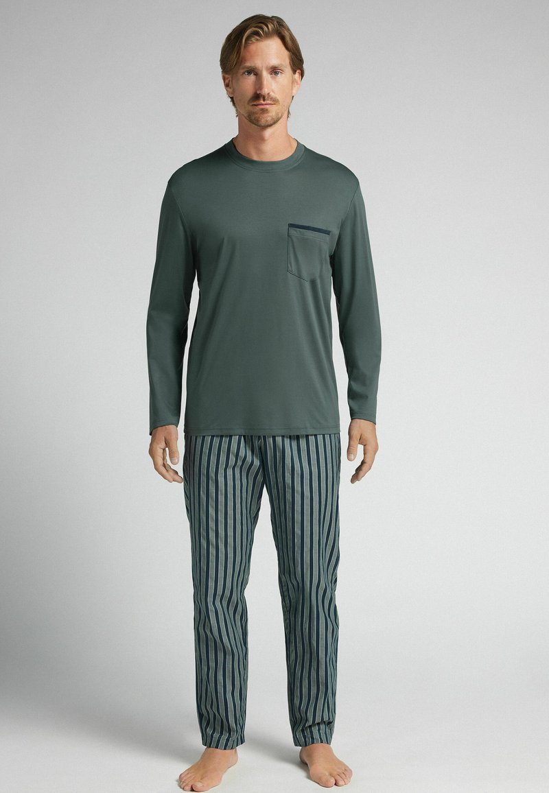 Dlouhý rukáv zeleného trika s kapsou na prsou v kombinaci s modrými a světle zelenými pruhovanými kalhotami. Měkká tkanina, uvolněný střih, jednoduchý design.