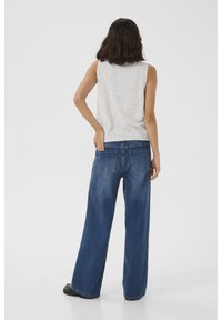 Top grigio senza maniche abbinato a jeans blu a gamba larga. I jeans presentano due tasche posteriori e una finitura sbiadita. Sono visibili anche calzature nere.