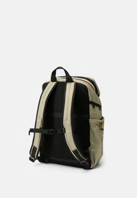 Sac à dos en kaki avec des bretelles en mesh noir, comportant plusieurs poches, une boucle réglable et une poignée de transport supérieure. Compartiment principal zippé.
