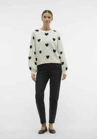 Pull crème avec motif de cœurs noirs, design court et manches bouffantes, associé à un jean noir ajusté et des ballerines noires.