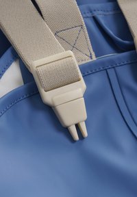 Blue waterproof material with beige straps. Close-up of a plastic buckle and tan stitching, featuring a smooth texture and minimal design.
