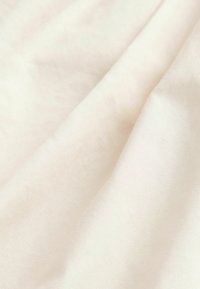Lys beige bomuldsstof med en glat, mat tekstur, der viser subtile folder og en ensartet overflade uden mønstre eller udsmykninger.