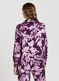 Blusa floreale viola con grandi motivi di piante rosa, maniche lunghe, colletto e vestibilità rilassata, realizzata in tessuto morbido.