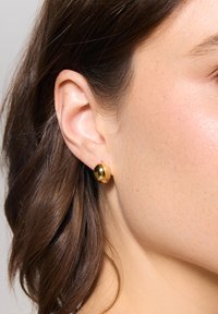 Złote kolczyki-stud w kolorze złotym o gładkiej, błyszczącej powierzchni. Są okrągłe i mają prosty, czysty design, idealny do codziennego noszenia.