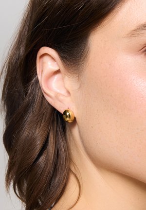 Złote kolczyki-stud w kolorze złotym o gładkiej, błyszczącej powierzchni. Są okrągłe i mają prosty, czysty design, idealny do codziennego noszenia.