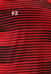 Punainen ja musta raidallinen urheilupaita, jossa on sileä pinta ja valkoinen "FZ"-logo vasemmassa yläkulmassa.