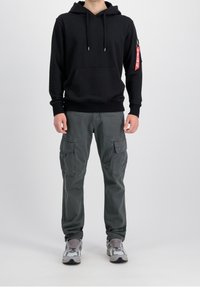 Sudadera negra con bolsillo frontal y cordones, combinada con pantalones cargo grises con bolsillos laterales, y finalizada con zapatillas grises y blancas.
