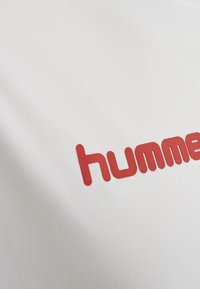 Hvid t-shirt med et markant rødt "humme" tekstlogo, med en glat overflade og et afslappet rund hals-design.