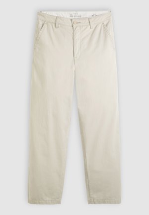 Gaismas bēša krāsas taisnu kāju chino bikses ar priekšējām kabatām, jostas cilpām, pogas aizdari un rāvējslēdzēja atvēršanu, izliktas plakani uz balta fona.