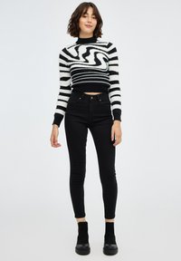 Suéter a rayas blanco y negro con un patrón de espiral, corte corto, combinado con jeans ajustados negros de cintura alta y botas negras hasta el tobillo.