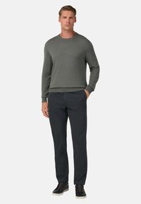 Sivý pletený sveter s textúrou, tmavé nohavice a čierne tenisky. Sveter má priehľadné manžety a spodný lem, s jednoduchým okrúhlym výstrihom.