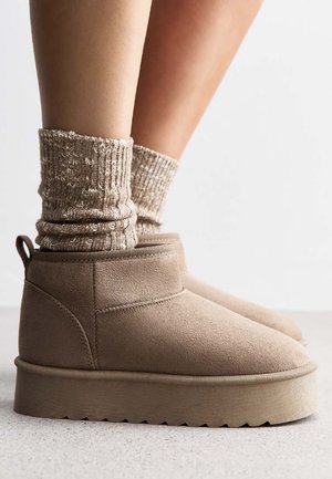 Beige Ankle-Boots aus Wildleder mit einer dicken, strukturierten Sohle. Getragen mit einer gefalteten, hellbraunen Rippensocke. Minimalistisches Design, keine Verzierungen.