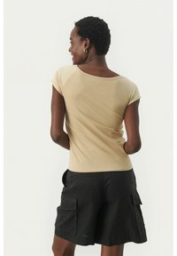 Beiges, tailliertes Oberteil mit rundem Ausschnitt, kurzen Ärmeln und glatter Textur, kombiniert mit dunklen Cargo-Shorts mit Seitentaschen.