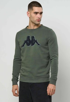 Grüner Pullover aus Baumwolle mit Rundhalsausschnitt und langen Ärmeln. Verziert mit einem schwarzen Grafikdesign auf der Brust.
