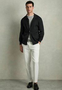 Cardigan negru cu nasturi, pulover gri dedesubt, pantaloni crem și pantofi negri. Materialul neted și croiul ajustat creează o siluetă curată.