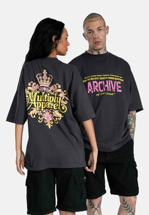 Sorte oversized t-shirts med markante grafikker: den ene har et krone-design i gul og pink, mens den anden har fed tekst i pink på ryggen.