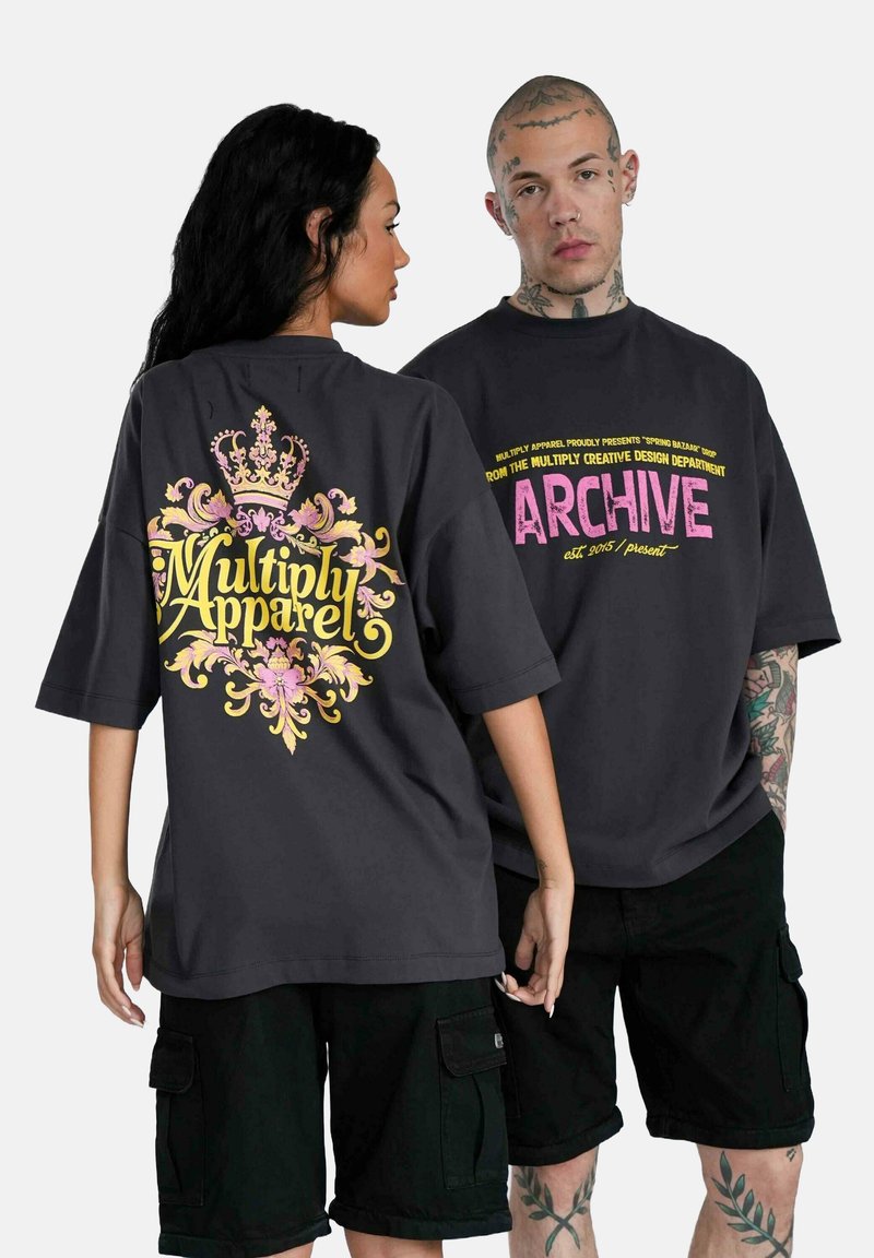 Camisetas negras de gran tamaño con gráficos distintivos: una presenta un diseño de corona en amarillo y rosa, la otra tiene un texto en negrita en rosa en la parte de atrás.