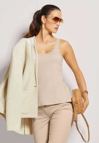 Beige Tanktop mit Spitzenbesatz, heller beiger Blazer, passende Hose und eine kleine tanfarbene Umhängetasche mit Quasten-Detail.