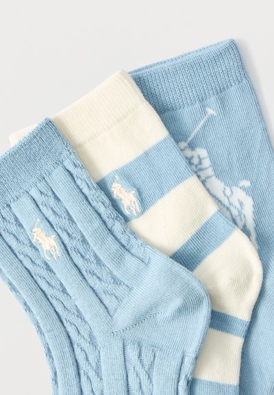 Τρία ζεύγη βρεφικών καλτσών σε ανοιχτό μπλε, λευκό και ριγέ σχέδια, με κεντημένα λογότυπα παικτών πόλο και λεπτομέρειες πλεκτού καλωδίου.