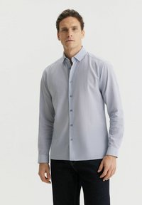 Jasnoniebieska, paskowana koszula na guziki z długimi rękawami, kołnierzykiem i niebieskimi guzikami. Noszona z ciemnymi dżinsami, o gładkiej fakturze.