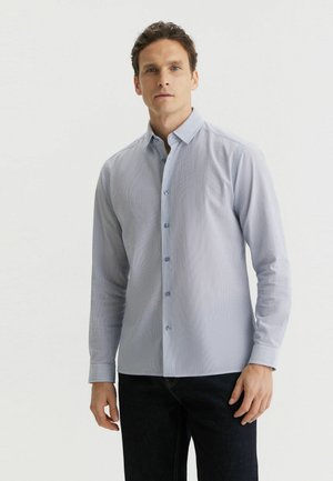 Jasnoniebieska, paskowana koszula na guziki z długimi rękawami, kołnierzykiem i niebieskimi guzikami. Noszona z ciemnymi dżinsami, o gładkiej fakturze.