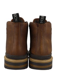 Botas de tobillo de cuero marrón con superficie texturizada, suela de goma en contraste y tiradores de marca negros en la parte trasera.