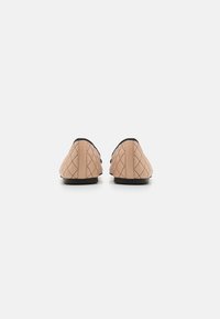 Chaussures à enfiler roses matelassées avec des accents noirs, présentant une texture lisse et des bouts arrondis, conçues pour un usage décontracté.