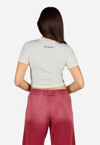 Īsām piedurknēm izgatavots pieguļošs krēmveidīgs T-krekls ar uzrakstu "PEGADOR" aizmugurē; kombinēts ar augstām rozā ombre biksēm ar elastīgu jostu.