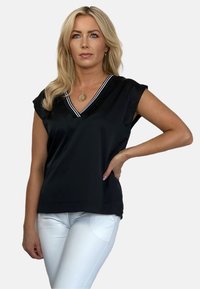 Czarna bluzka z dekoltem w serek i krótkimi rękawami, z kontrastującym białym paskiem na dekolcie. Gładka tekstura, luźny krój, zestawiona z białymi spodniami.