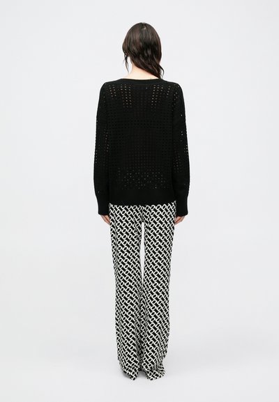 Čierny pletený sveter voľného strihu s textúrovaným otvoreným vzorom. Kombinovaný so širokými nohavicami v čierno-bielom geometrickom vzore.