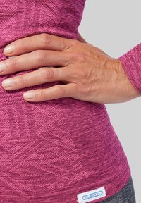 Strakke paarse textieltop met een gemarmerd patroon, met een zichtbaar gestikt merkje aan de onderkant en een close-up van een hand die erop rust.