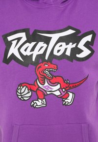 Raptor rouge portant des chaussures et un maillot de basket-ball, dribblant un ballon sous le mot Raptors en lettres blanches grasses sur fond violet.