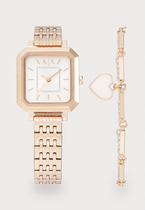 Montre en or rose avec un cadran carré et un bracelet en maille, accompagnée d'un bracelet assorti avec un charm en forme de cœur. Cadran blanc avec accents roses.