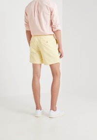 Světlé žluté bavlněné šortky s elastickým pasem, zadními kapsami a hladkou texturou, spárované s dlouhým rukávem pruhovaným růžovým tričkem.