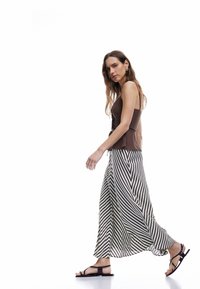 Bruine fitted tanktop met verstelbare bandjes, gecombineerd met een vloeiende, gestreepte zwart-witte maxi rok en zwarte sandalen.