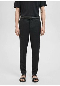 Zwarte rechte broek met een gladde textuur, rechte snit en een subtiele glans. Gecombineerd met zwarte sandalen en een donker shirt met korte mouwen.