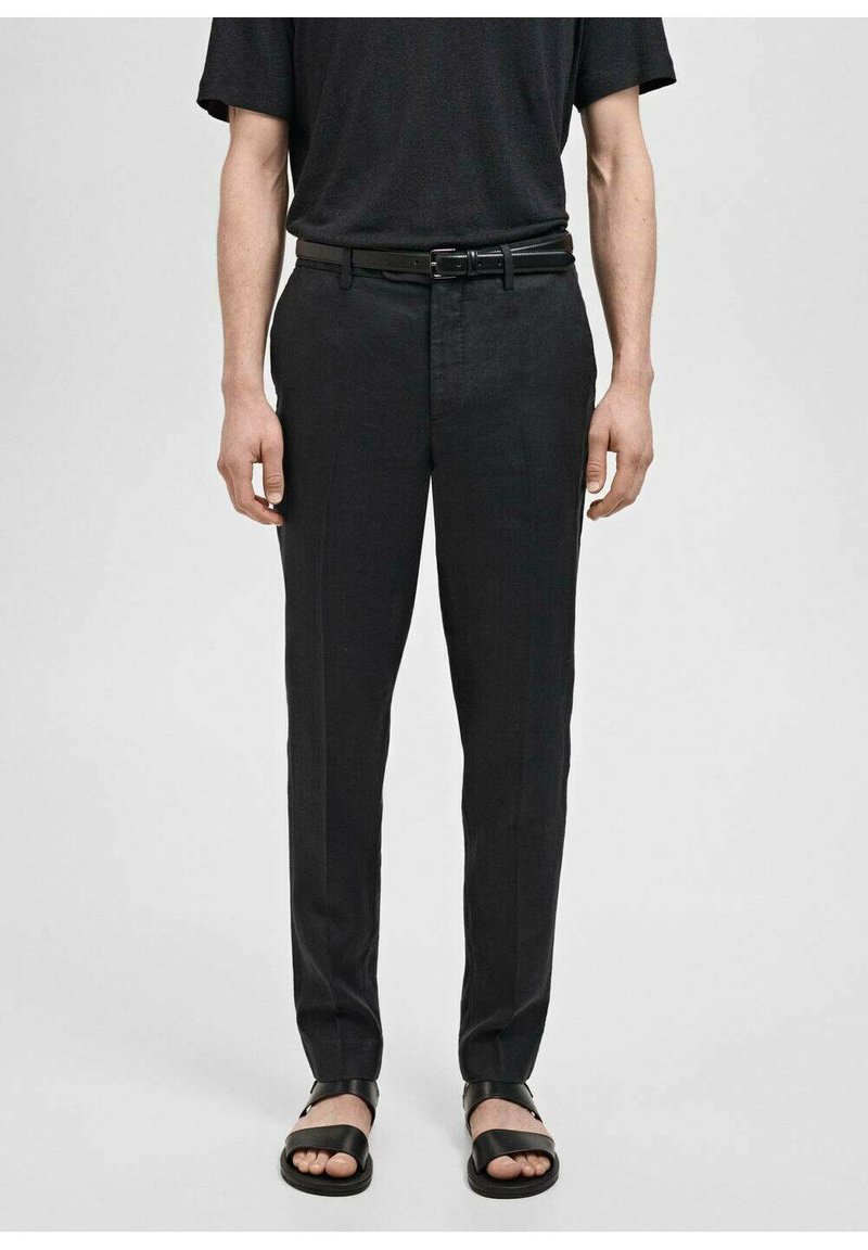 Zwarte rechte broek met een gladde textuur, rechte snit en een subtiele glans. Gecombineerd met zwarte sandalen en een donker shirt met korte mouwen.
