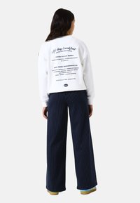 White sweatshirt with graphic text on the back, paired with navy pinstriped pants and colorful footwear. Casual streetwear design.