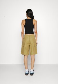 Débardeur noir court associé à un short cargo kaki. Le short est doté de poches latérales et d'une taille élastique. Porté avec des chaussettes blanches et des baskets bleues.