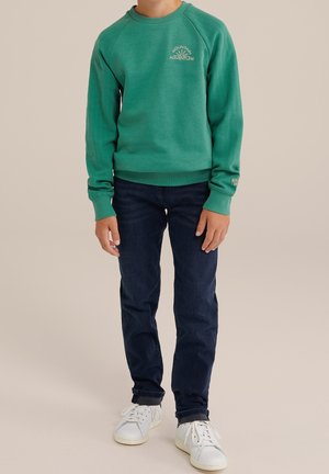 Grøn sweatshirt med ribbet tekstur og rund halsudskæring, med trykket "MOUNTAIN ADVENTURE". Kombineret med mørkeblå jeans og hvide sneakers.
