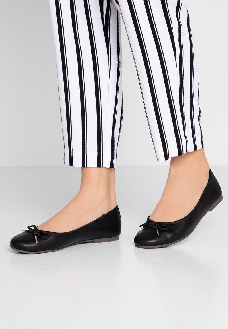 Svarta balettlägenheter med en slät yta, rund tå och liten rosettdetalj framtill; använda tillsammans med vita och svarta randiga, korta byxor.