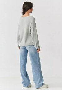 Jasnoszary, oversize sweter o teksturowym wykończeniu, w połączeniu z wysokim stanem, szerokimi dżinsami w jasnym odcieniu. Widoczne płaskie buty.